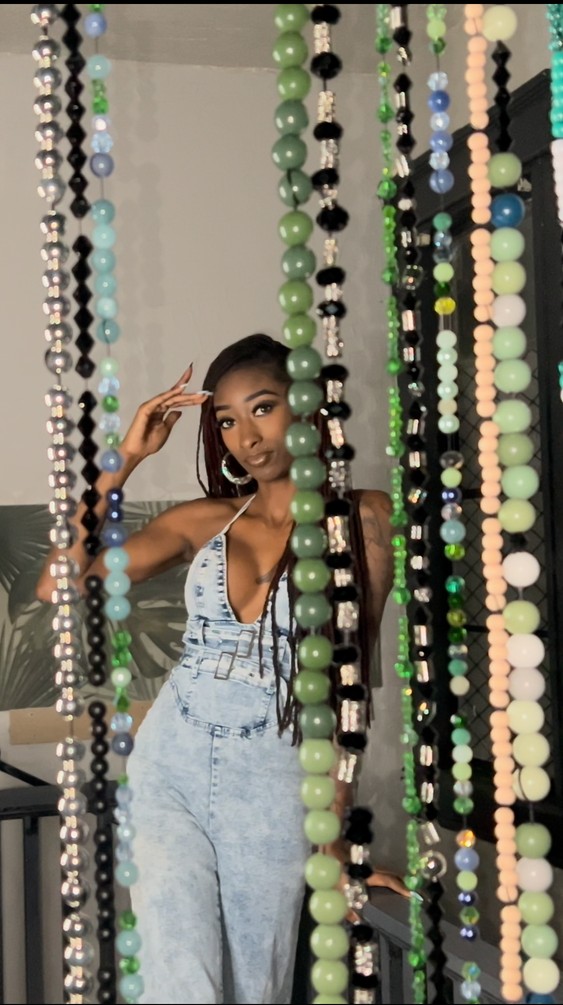 Woman with long locs standing among beaded curtains